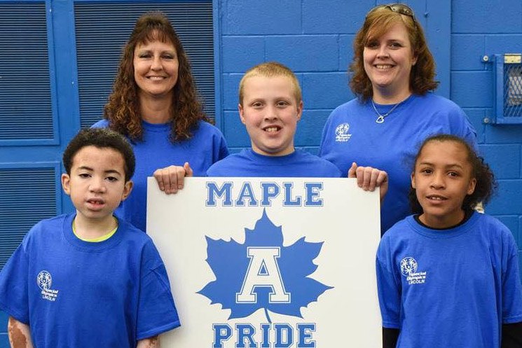 Adults and students smiling holding up a Maple sign.